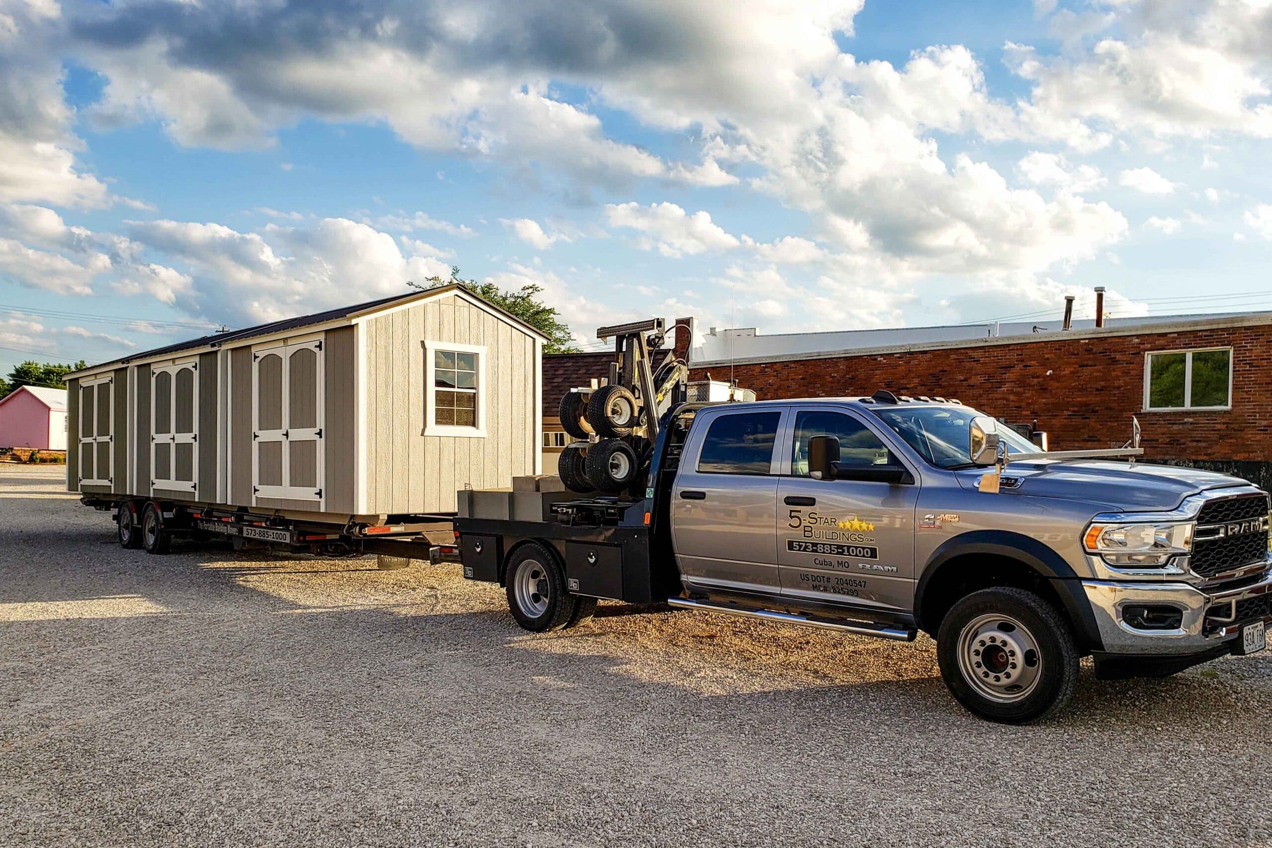 We deliver sheds to Sullivan MO - Gray pickup truck towing gray and white sheds to property private road flanked by sparse trees