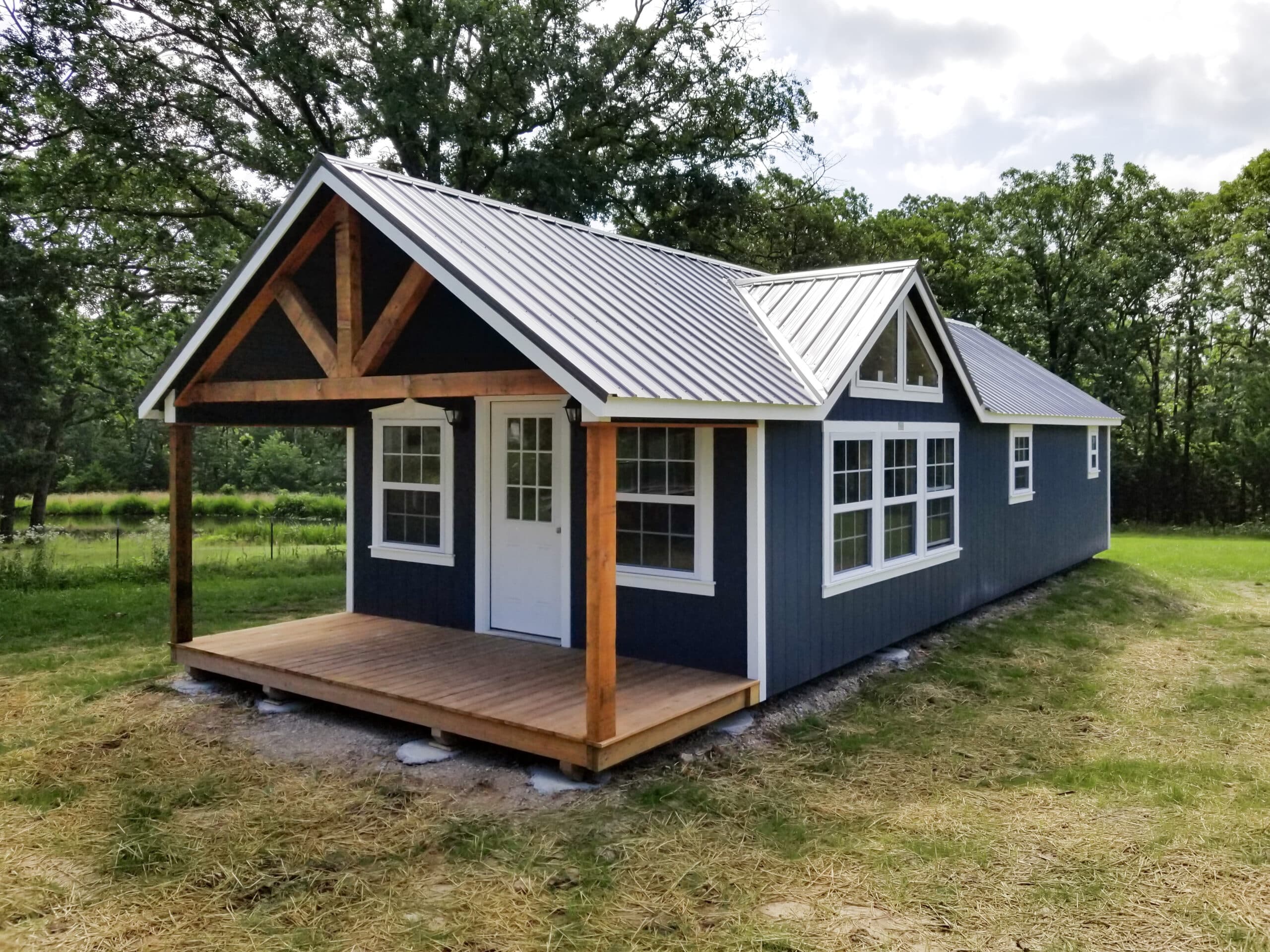 One of our red lofted cabins sheds for sale in Sullivan MO- Red siding whith fenced porch four visible white windows and windowed door beneath metal gray roof