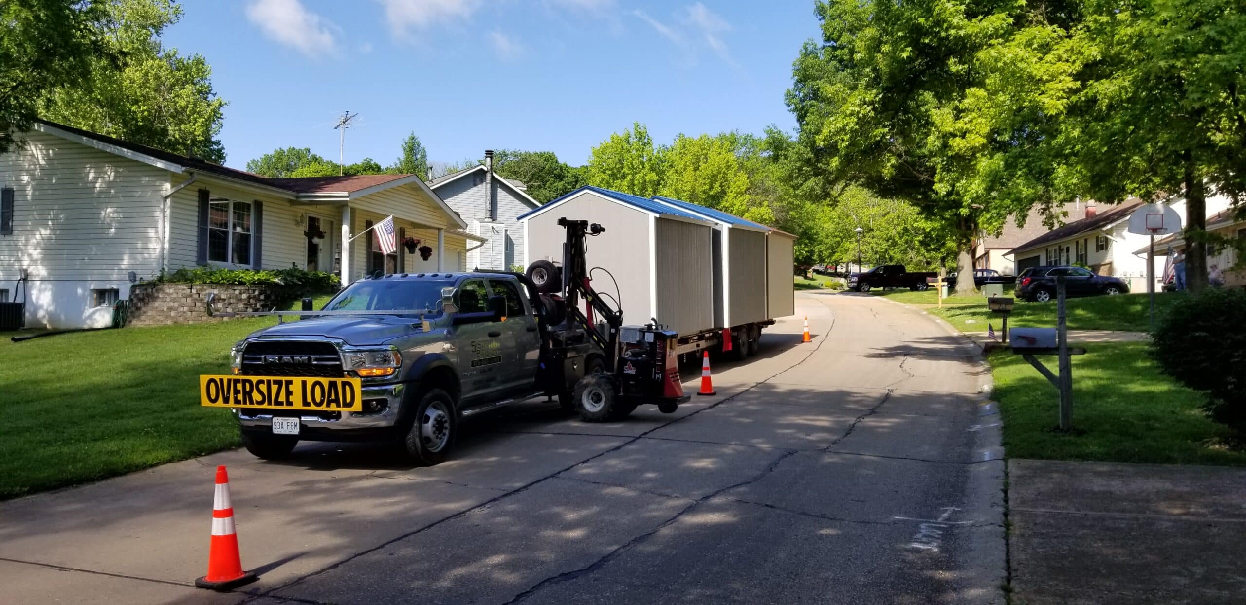 We deliver sheds to Sullivan MO - Gray pickup truck towing gray and white sheds to property private road flanked by sparse trees