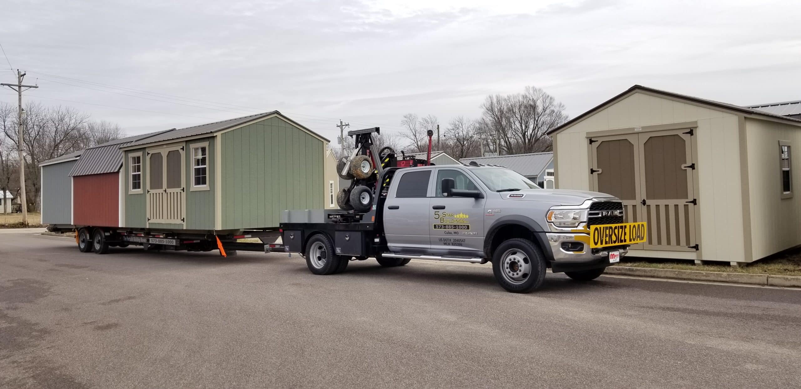 We deliver sheds to Sullivan MO - Gray pickup truck towing gray and white sheds to property private road flanked by sparse trees