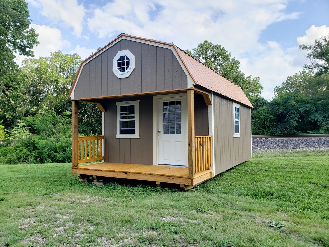 Tan with wooden porch, white windows and doors beneath bronze metal roof. Just one of our popular cabins for sale near Washington MO