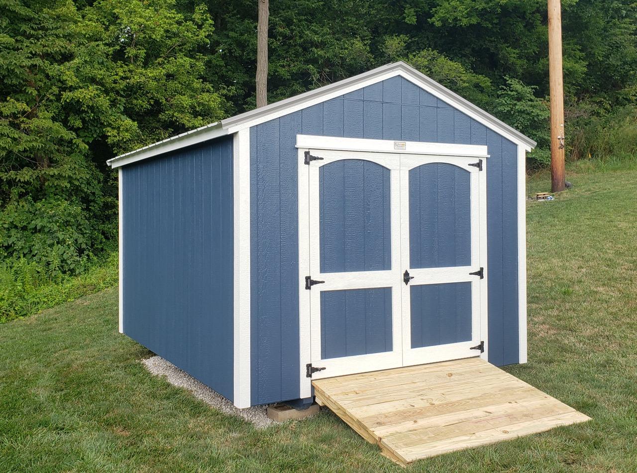 one of our blue and white portable buildings for sale near Washington MO - Utility shed with blue siding and white trimmed doors and corners beneath Gable style roof - shed shits on grass near lush trees